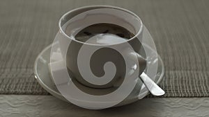 Close up white cup black coffee with sugar and spoon on saucer standing on table