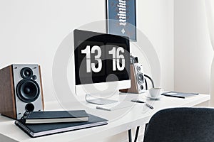 Close-up of a white desk with spiral notepads, speakers and a modern desktop computer in a stylish workspace interior with white w photo