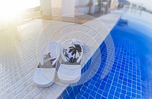 close up of a white flip flop with surfer motifs on the edge of an infinity pool at sunset, with a chill out bar in the background