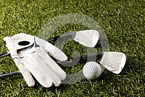 Close up of white glove, golf ball and golf clubs on grass with copy space