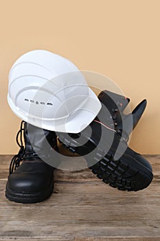 Close-up of white hardhat, pair of new black work boots made of leather with reinforced cape on old wooden boards, concept of