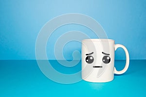 Close-up of a white mug on a blue background looking sad.