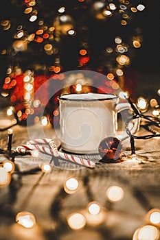 Close up of a white mug with christmas lights and christmas decorations ona wooden table