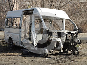 Close-up of a white old rusty van with broken windows, no engine in the background of the forest, awaiting dismantling