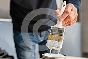 Close up on white paint brush in the hand of unknown man hobby painting and renovation repairing concept