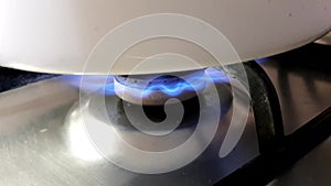 Close-up of a white pan on a gas stove with a burning blue flame