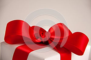 Close up of white paper gift box with a red satin ribbon bow on bright background. Holidays greeting cards and Christmas shopping