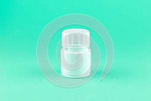 Close up white pill bottle on aquamarine background with copy space. Focus on foreground, soft bokeh. Pharmacy drugstore concept