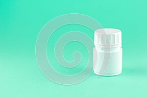 Close up white pill bottle on aquamarine background with copy space. Focus on foreground, soft bokeh. Pharmacy drugstore concept