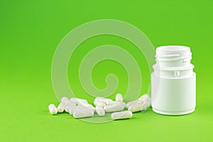 Close up white pill bottle with spilled out capsules on green background with copy space. Focus on foreground, soft bokeh. Pharmac