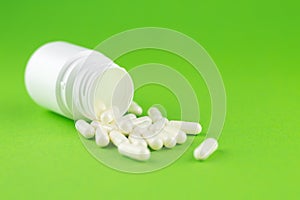 Close up white pill bottle with spilled out capsules on green background with copy space. Focus on foreground, soft bokeh. Pharmac