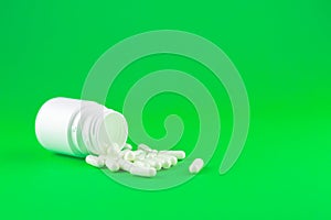 Close up white pill bottle with spilled out capsules on lime green background with copy space. Focus on foreground, soft bokeh. Ph