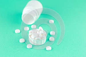 Close up white pill bottle with spilled out pills and capsules in cap on aquamarine background with copy space. Focus on foregroun