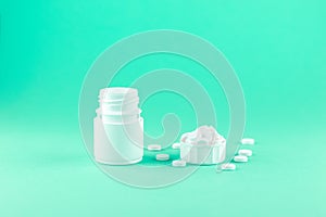 Close up white pill bottle with spilled out pills and capsules in cap on aquamarine background with copy space. Focus on foregroun