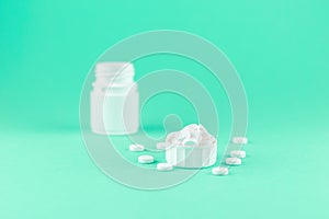 Close up white pill bottle with spilled out pills and capsules in cap on aquamarine background with copy space. Focus on foregroun