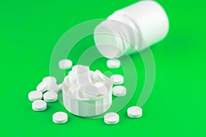 Close up white pill bottle with spilled out pills and capsules in cap on lime green background with copy space. Focus on foregroun