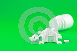 Close up white pill bottle with spilled out pills and capsules in cap on lime green background with copy space. Focus on foregroun