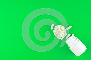 Close up white pill bottle with spilled out pills and capsules in cap on lime green background with copy space. Focus on foregroun