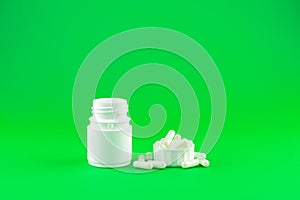 Close up white pill bottle with spilled out pills and capsules in cap on lime green background with copy space. Focus on foregroun