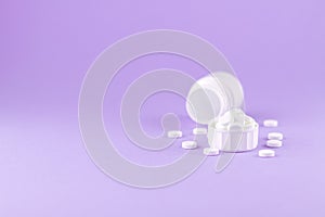 Close up white pill bottle with spilled out pills and capsules in cap on purple background with copy space. Focus on foreground, s