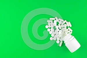 Close up white pill bottle with spilled out pills and capsules on lime green background with copy space. Focus on foreground, soft