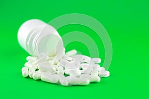 Close up white pill bottle with spilled out pills and capsules on lime green background with copy space. Focus on foreground, soft