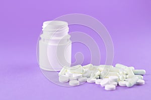 Close up white pill bottle with spilled out pills and capsules on purple background with copy space. Focus on foreground, soft bok