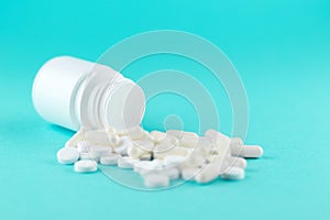 Close up white pill bottle with spilled out pills and capsules on turquoise background with copy space. Focus on foreground, soft