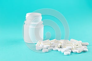 Close up white pill bottle with spilled out pills and capsules on turquoise background with copy space. Focus on foreground, soft