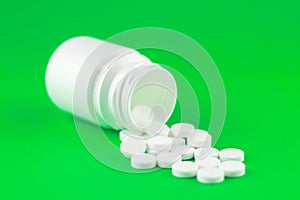 Close up white pill bottle with spilled out pills on lime green background with copy space. Focus on foreground, soft bokeh. Pharm