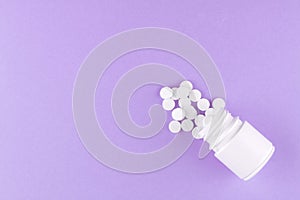 Close up white pill bottle with spilled out pills on purple background with copy space. Focus on foreground, soft bokeh. Pharmacy