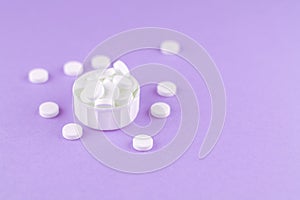 Close up white pills and capsules in cap on purple background with copy space. Focus on foreground, soft bokeh. Pharmacy drugstore