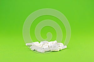 Close up white pills and capsules on green background with copy space. Focus on foreground, soft bokeh. Pharmacy drugstore concept