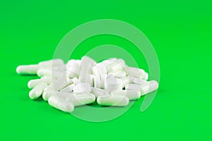 Close up white pills and capsules on lime green background with copy space. Focus on foreground, soft bokeh. Pharmacy drugstore co