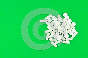 Close up white pills and capsules on lime green background with copy space. Focus on foreground, soft bokeh. Pharmacy drugstore co