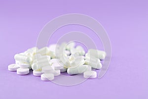 Close up white pills and capsules on purple background with copy space. Focus on foreground, soft bokeh. Pharmacy drugstore concep