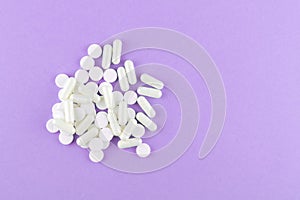 Close up white pills and capsules on purple background with copy space. Focus on foreground, soft bokeh. Pharmacy drugstore concep