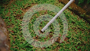 Close-up of a white pipe lying on vibrant green grass with visible soil and foliage textures