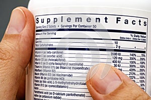 Close-up of white plastic jar with supplement facts of multivitamins in hands