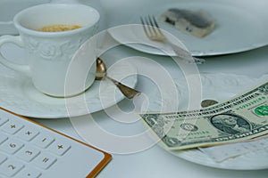 Close-up of white plate for money, American dollars banknotes and coins, Restaurant bill, cup of coffee, delicate pink flowers,