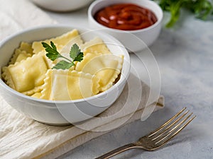 Close-up is a white plate with mouth-watering ravioli garnished with a sprig of parsley. Also in the frame is a gravy boat with