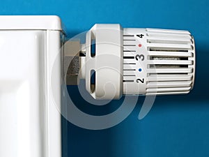 Close-up of a white radiator thermostat on a blue background, conceptual image for rising heating bills