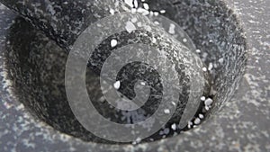 Close-up of a white sea salt falling on the pestle in the grey stone mortar