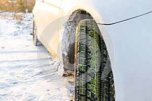 Close up of white sedan car tire tread wheel with green grass on a winter countryside road  nature landscape covered in snow