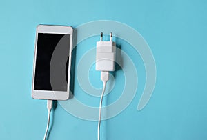 Close up white Smartphone Plug In with Charger Adapter on Blue Background