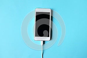 Close up white Smartphone Plug In with Charger Adapter on Blue Background