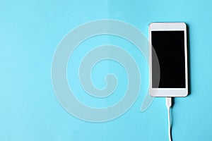 Close up white Smartphone Plug In with Charger Adapter on Blue Background