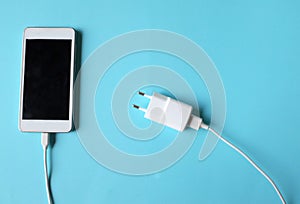 Close up white Smartphone Plug In with Charger Adapter on Blue Background