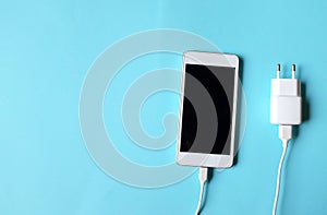 Close up white Smartphone Plug In with Charger Adapter on Blue Background