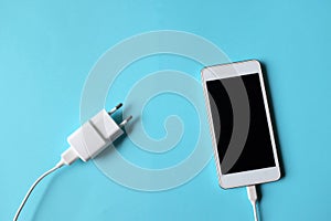 Close up white Smartphone Plug In with Charger Adapter on Blue Background